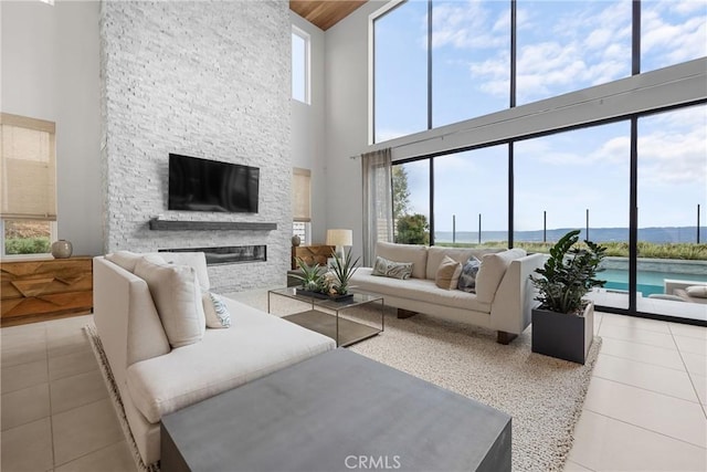 living room featuring light tile patterned floors, a stone fireplace, a healthy amount of sunlight, and a high ceiling