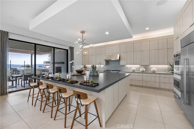 kitchen with a breakfast bar area, hanging light fixtures, light tile patterned floors, a large island, and backsplash