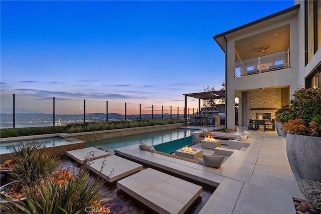 pool at dusk featuring an outdoor fire pit, ceiling fan, a pergola, a water view, and a patio area