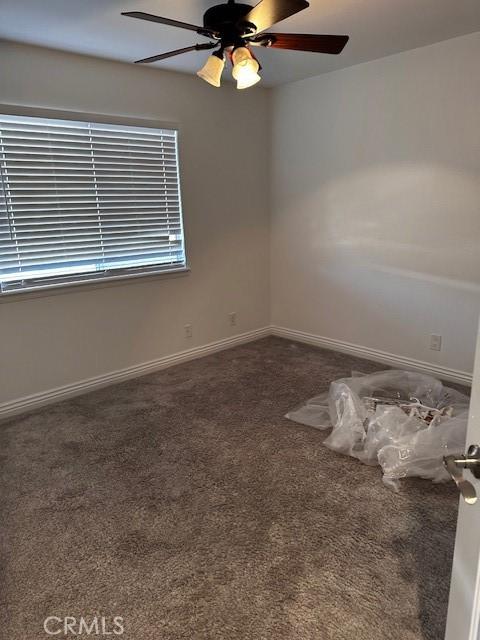 unfurnished room with ceiling fan and dark colored carpet