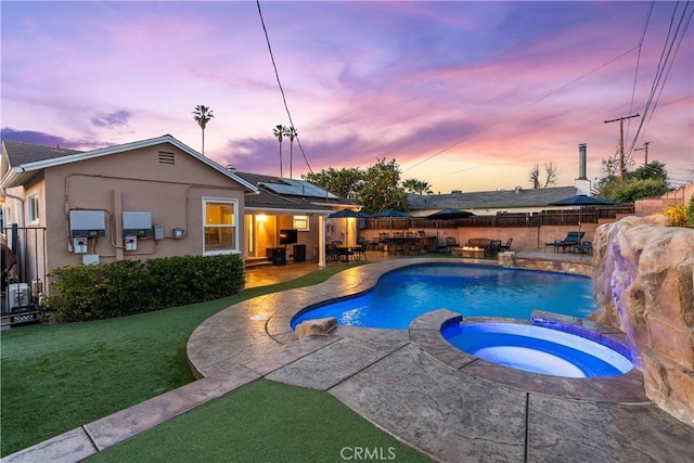 pool at dusk with an in ground hot tub, a lawn, and a patio