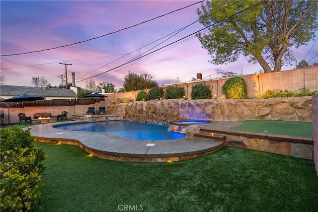 pool at dusk featuring a yard, an outdoor fire pit, and an in ground hot tub