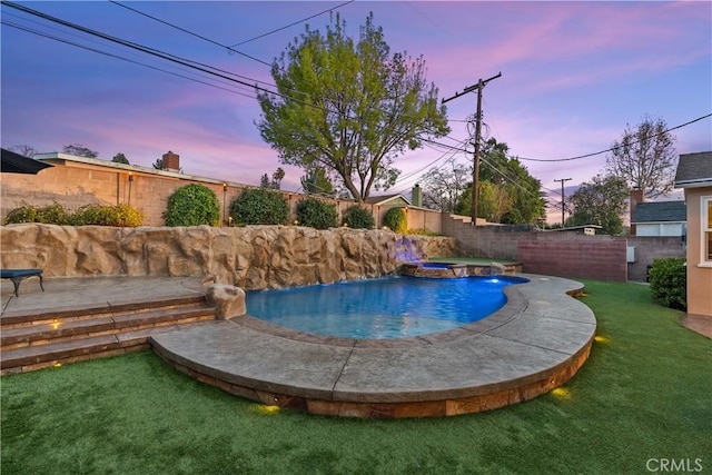 pool at dusk with a yard, pool water feature, and an in ground hot tub