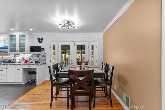 dining room with french doors, ornamental molding, a chandelier, and light wood-type flooring