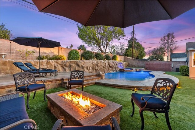 patio terrace at dusk featuring a swimming pool with hot tub, a fire pit, and a lawn