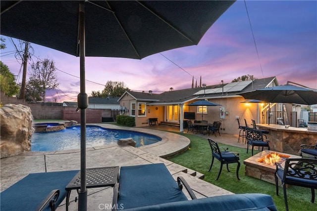 pool at dusk featuring an in ground hot tub, a patio, an outdoor bar, and a fire pit