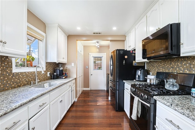 kitchen with light stone counters, black range with gas stovetop, sink, and white cabinets