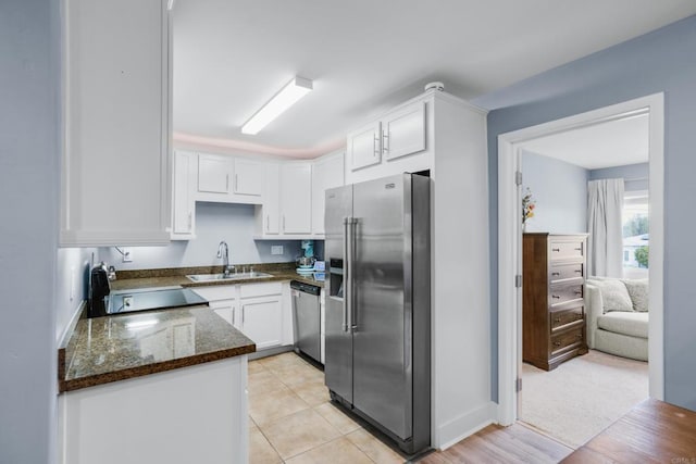 kitchen featuring light tile patterned floors, appliances with stainless steel finishes, dark stone countertops, white cabinetry, and a sink