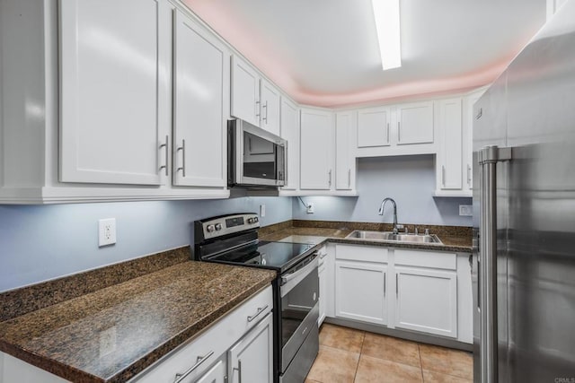 kitchen with appliances with stainless steel finishes, light tile patterned flooring, a sink, and white cabinets