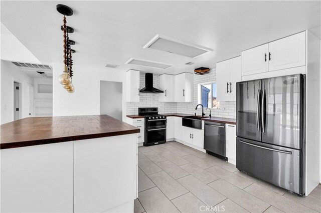 kitchen with appliances with stainless steel finishes, butcher block countertops, sink, white cabinets, and wall chimney range hood