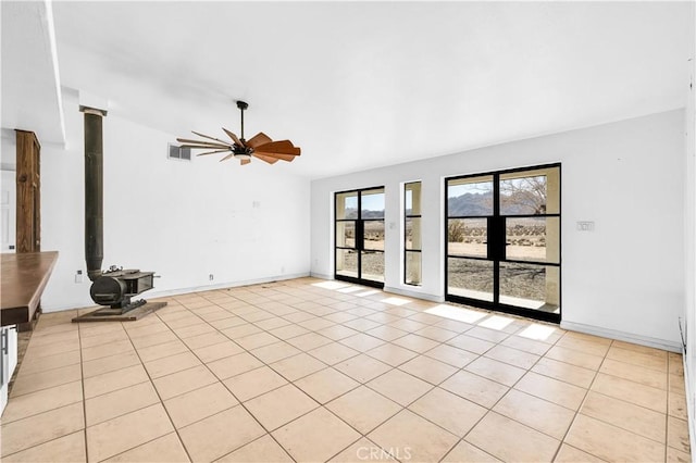 unfurnished living room featuring a wood stove, light tile patterned floors, and ceiling fan