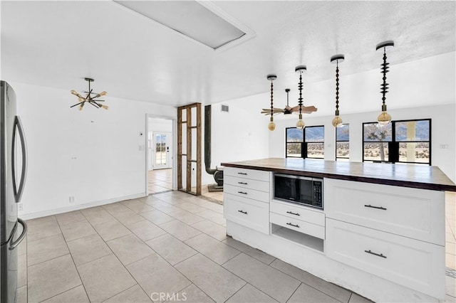 kitchen with wood counters, black microwave, hanging light fixtures, stainless steel fridge, and white cabinets