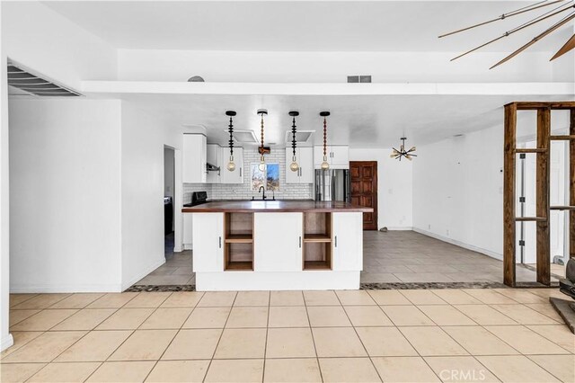 kitchen with light tile patterned flooring, white cabinetry, hanging light fixtures, stainless steel refrigerator, and decorative backsplash