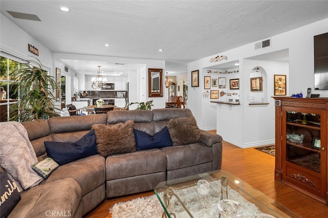 living room with a notable chandelier, a textured ceiling, and light wood-type flooring