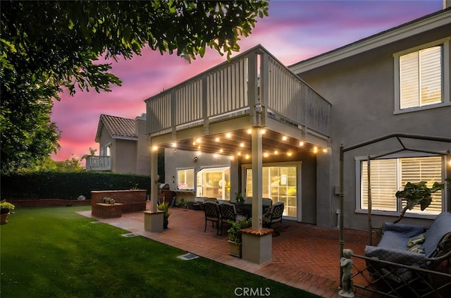 back house at dusk with a lawn, outdoor lounge area, a patio, and a balcony