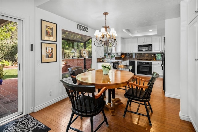 dining area with a raised ceiling, a wealth of natural light, an inviting chandelier, and light hardwood / wood-style flooring