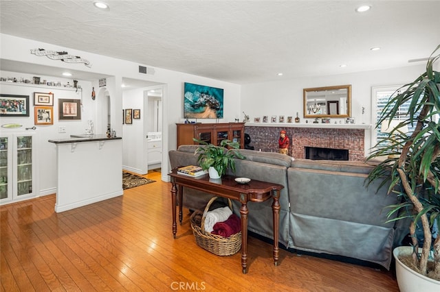 living room with a brick fireplace, light hardwood / wood-style flooring, a textured ceiling, and indoor bar