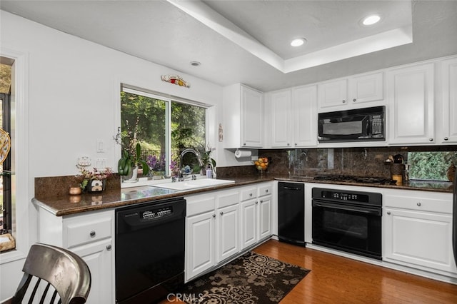 kitchen with dark wood-type flooring, sink, black appliances, a tray ceiling, and white cabinets