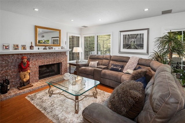 living room featuring a brick fireplace, wood-type flooring, and a textured ceiling