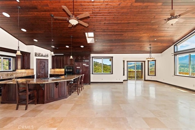 kitchen featuring paneled refrigerator with ice dispenser, a kitchen breakfast bar, hanging light fixtures, ceiling fan, and light stone counters