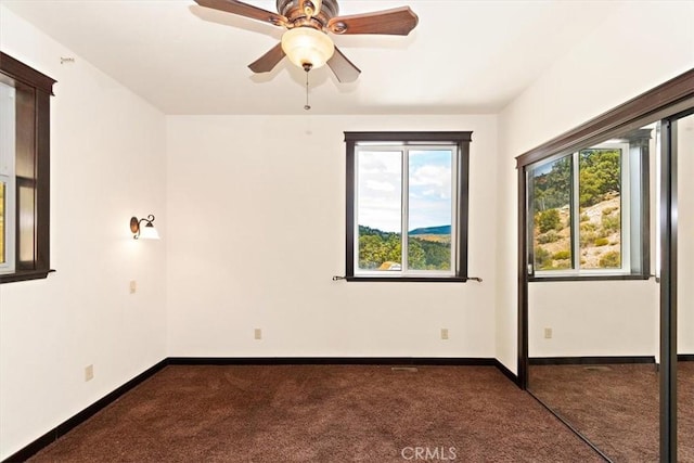 empty room featuring ceiling fan and dark carpet