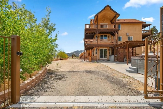 back of property featuring a balcony, a hot tub, a mountain view, and a patio area