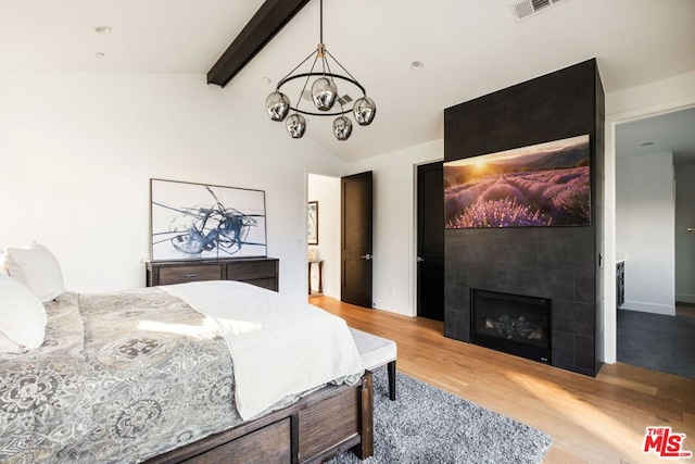 bedroom with a tiled fireplace, vaulted ceiling with beams, an inviting chandelier, and light hardwood / wood-style floors