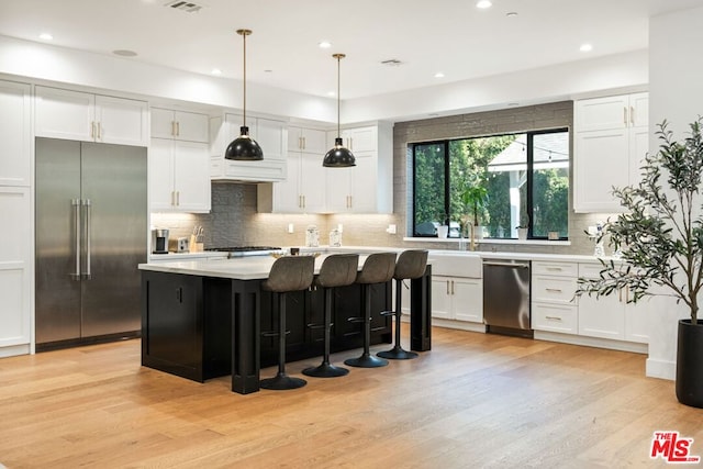 kitchen featuring white cabinetry, appliances with stainless steel finishes, a kitchen island, pendant lighting, and light hardwood / wood-style floors