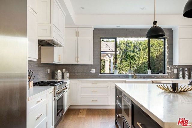 kitchen featuring appliances with stainless steel finishes, white cabinetry, hanging light fixtures, tasteful backsplash, and light hardwood / wood-style floors