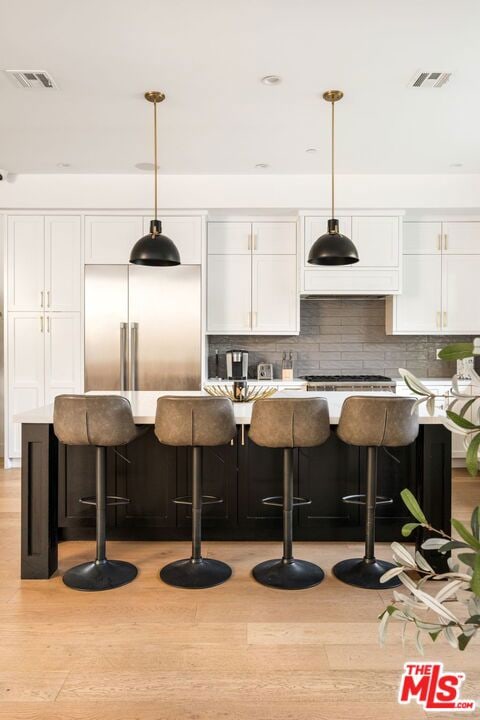 bar featuring stainless steel appliances, white cabinets, light hardwood / wood-style floors, and decorative light fixtures