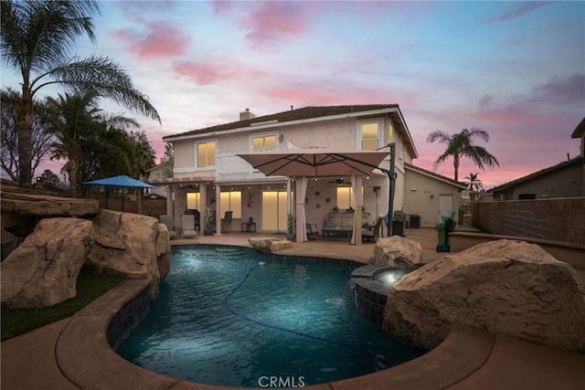 back house at dusk with a fenced in pool, a balcony, a patio, and pool water feature