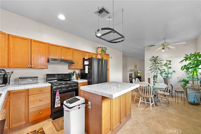 kitchen featuring a center island, light tile patterned floors, tile counters, ceiling fan, and black appliances