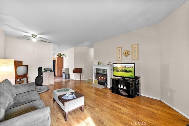 living room featuring a tiled fireplace, light hardwood / wood-style flooring, and ceiling fan