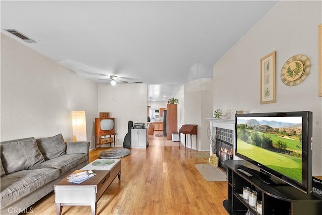 living room with ceiling fan, a fireplace, and light hardwood / wood-style flooring