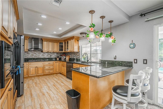 kitchen featuring kitchen peninsula, hanging light fixtures, black appliances, a raised ceiling, and wall chimney range hood