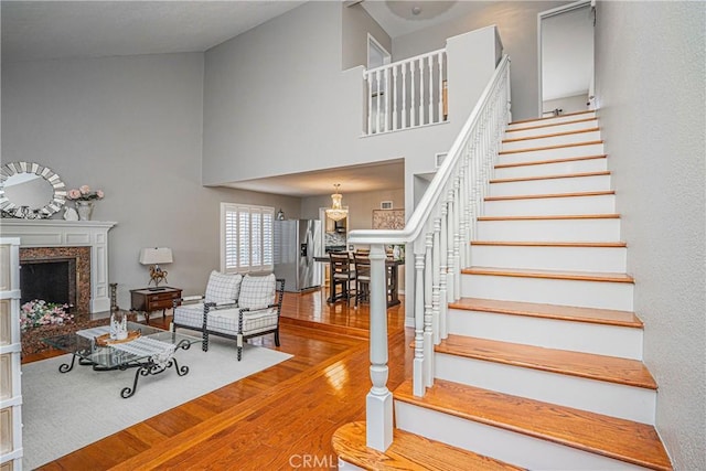 staircase with hardwood / wood-style floors, a premium fireplace, and a high ceiling