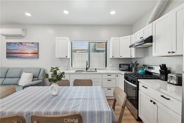 kitchen featuring stainless steel gas range, sink, white cabinetry, a wall mounted air conditioner, and light stone countertops