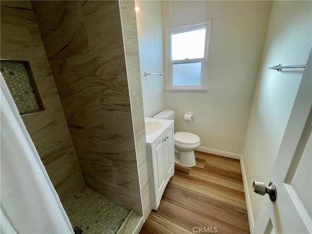 bathroom with tiled shower, wood-type flooring, toilet, and vanity