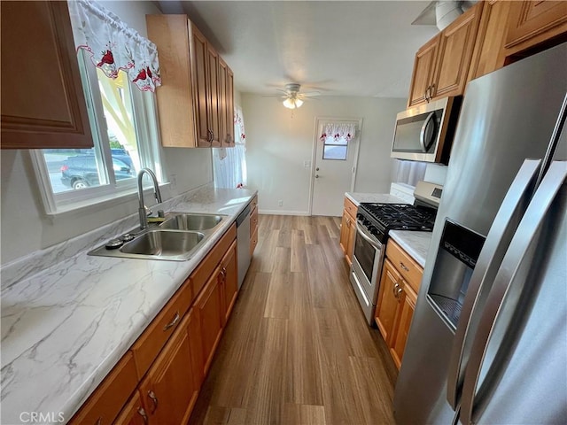 kitchen with appliances with stainless steel finishes, sink, ceiling fan, and light hardwood / wood-style flooring