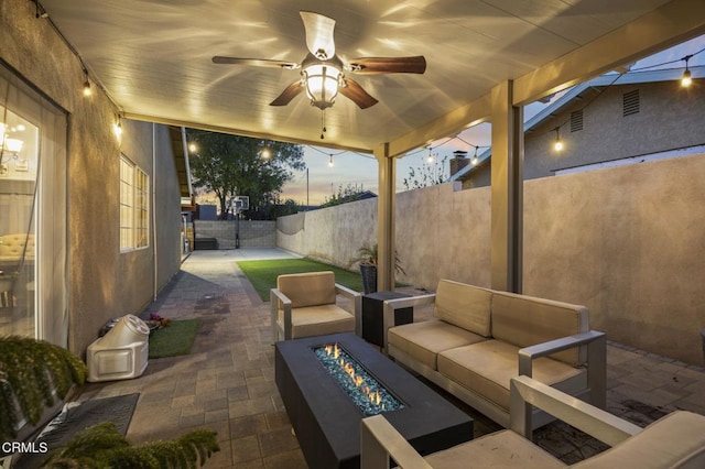 patio terrace at dusk featuring ceiling fan and an outdoor living space with a fire pit