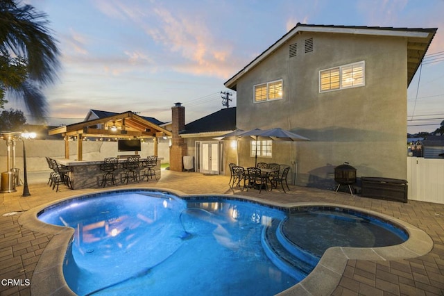 pool at dusk featuring a gazebo, a patio area, and exterior bar