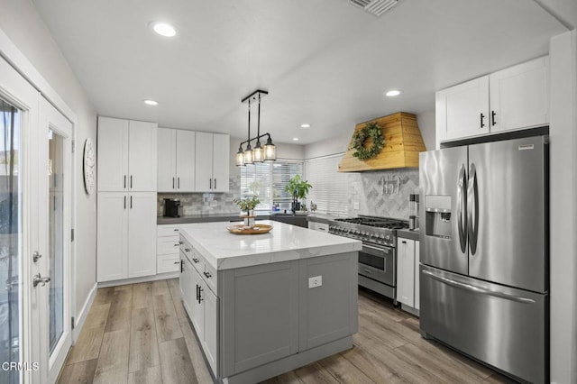 kitchen with pendant lighting, appliances with stainless steel finishes, custom range hood, white cabinets, and a kitchen island