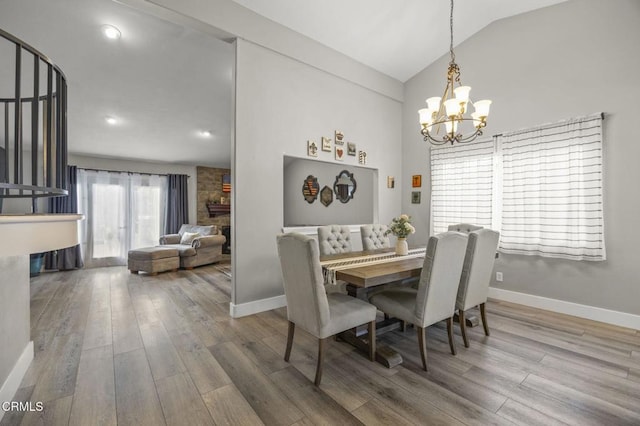 dining area with vaulted ceiling, hardwood / wood-style floors, a notable chandelier, and a fireplace