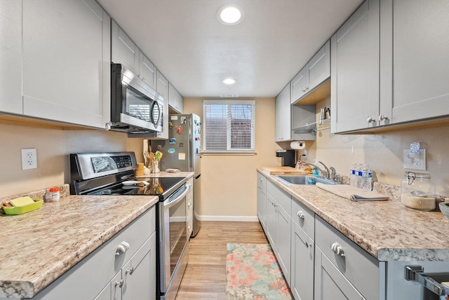 kitchen featuring sink, stainless steel appliances, light hardwood / wood-style floors, and light stone countertops