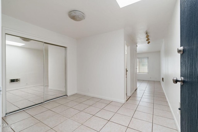 unfurnished bedroom featuring rail lighting, light tile patterned floors, a closet, and a skylight