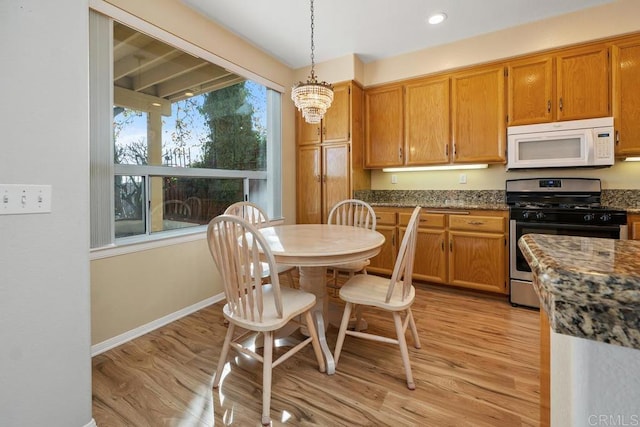 kitchen featuring light hardwood / wood-style flooring, decorative light fixtures, stainless steel gas range, and dark stone counters