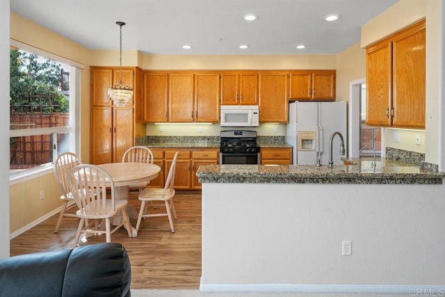 kitchen with dark stone countertops, hanging light fixtures, white appliances, and light hardwood / wood-style flooring