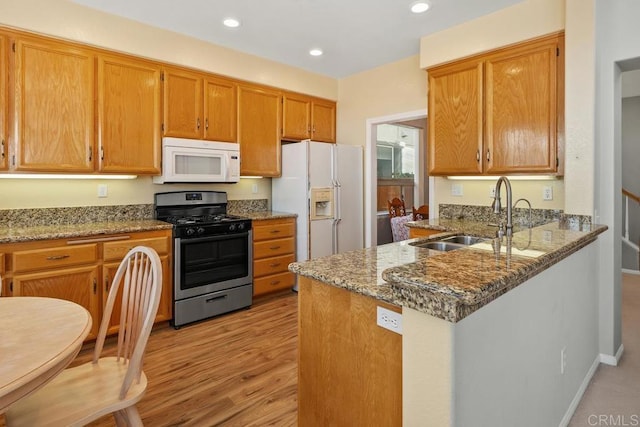 kitchen featuring light stone counters, sink, white appliances, and kitchen peninsula