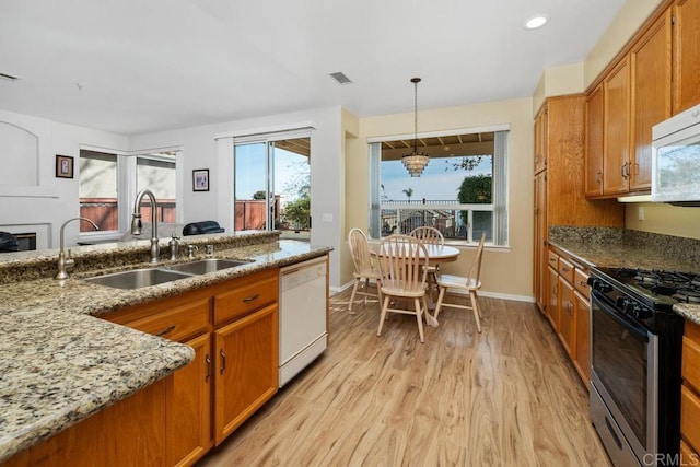 kitchen with sink, light stone counters, light hardwood / wood-style flooring, pendant lighting, and white appliances