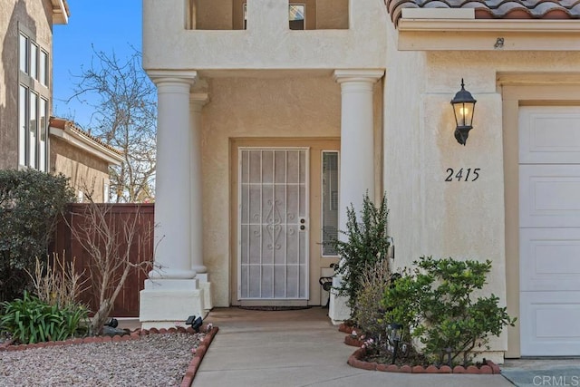 entrance to property featuring a garage, fence, a tiled roof, and stucco siding